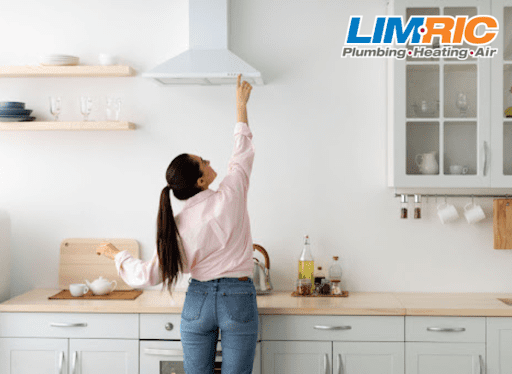 A woman turning on the exhaust fan in a kitchen.